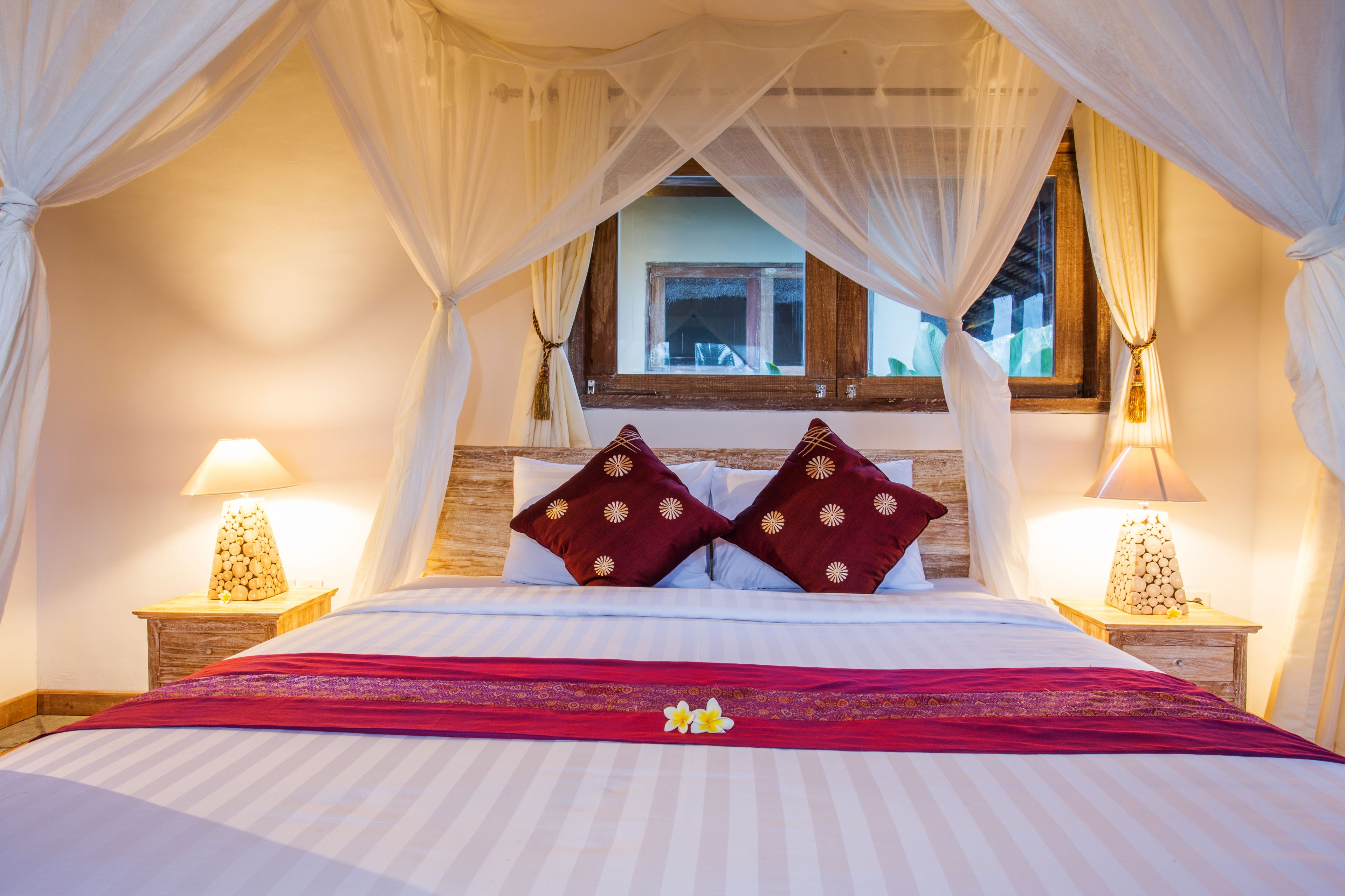 A bed with a canopy, two pillows, a red bedspread, and two bedside lamps.