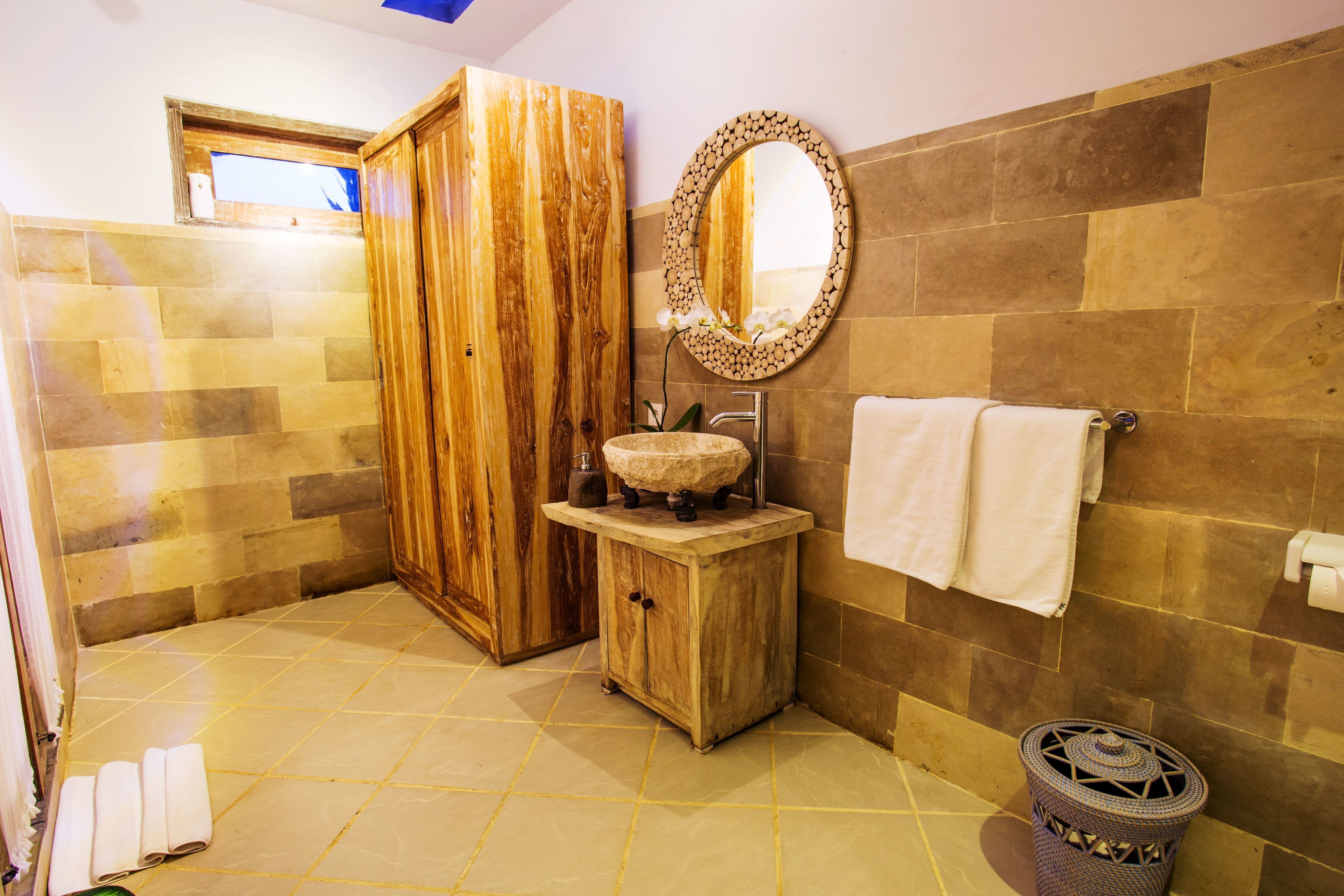 Une salle de bain avec un meuble en bois, un miroir rond, un lavabo et un porte-serviettes.