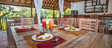 Uma mesa de jantar de madeira com pratos de comida e bebidas, rodeada por cadeiras de madeira.