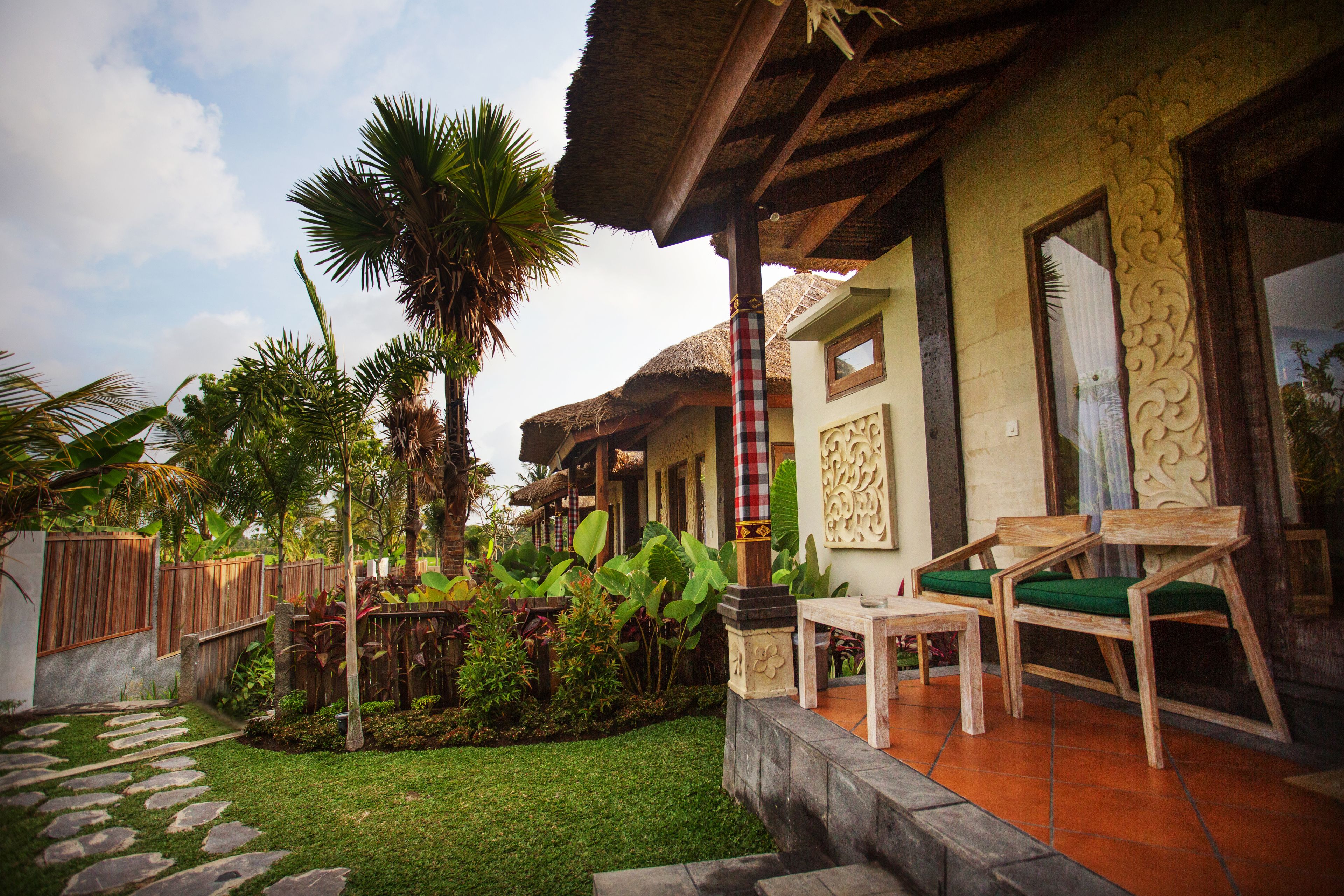 A tropical-style house with a thatched roof, a small garden with palm trees, and wooden furniture.