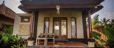 A traditional house with a thatched roof, a wooden porch, and a small garden area.
