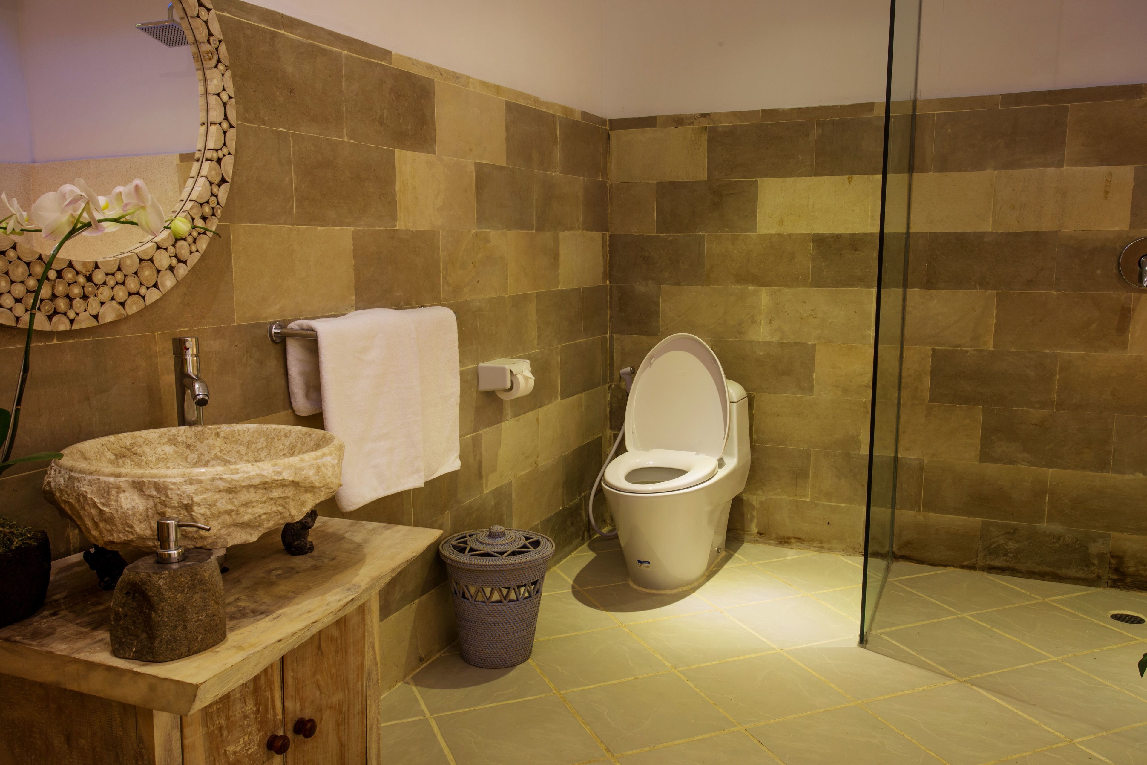 Ein Badezimmer mit einem Steinkonstruktion als Waschbecken, einer Toilette und einer Duschkabine aus Glas.