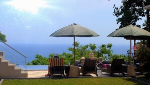 An outdoor seating area with two umbrellas, chairs, and a view of the ocean. - Villa Karingal (Senggigi)