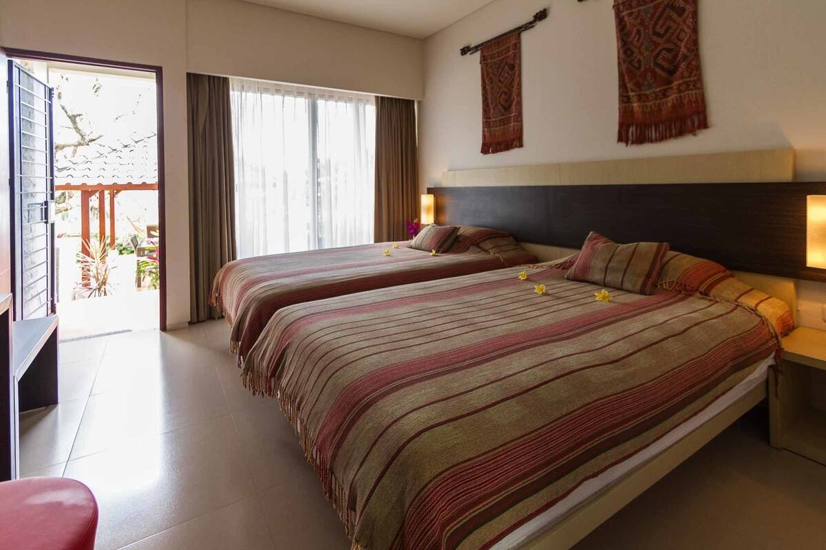 A hotel room with two beds, a desk, and a balcony with a view.