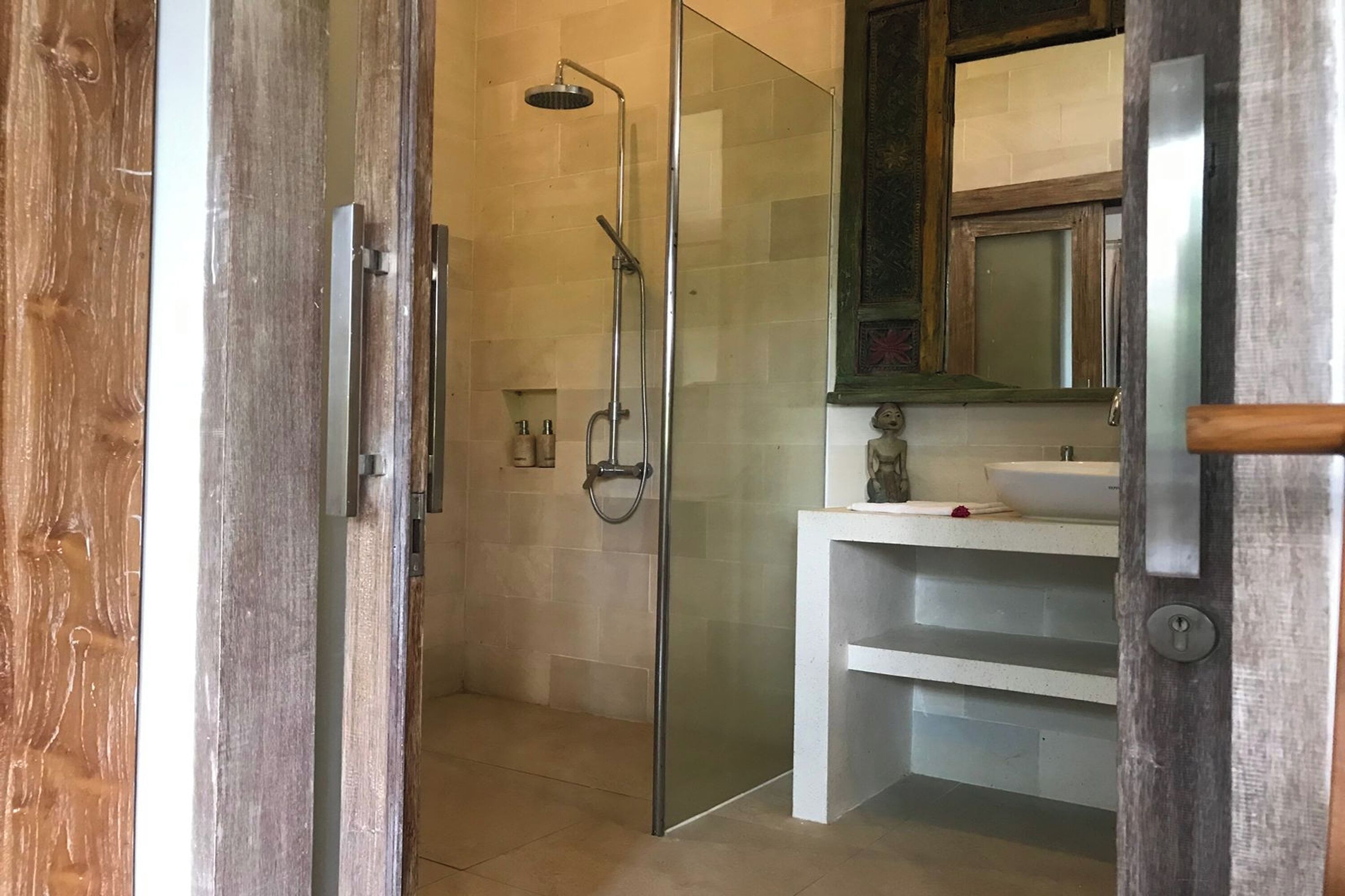 A modern bathroom with a glass-enclosed shower, a white sink, and a wooden door.