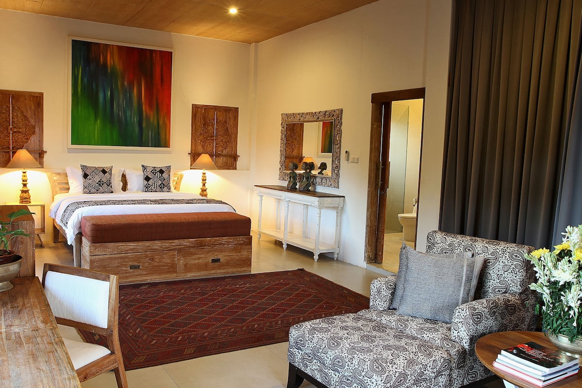A bedroom with a bed, bedside tables, a sofa, a mirror, and a large abstract painting.
