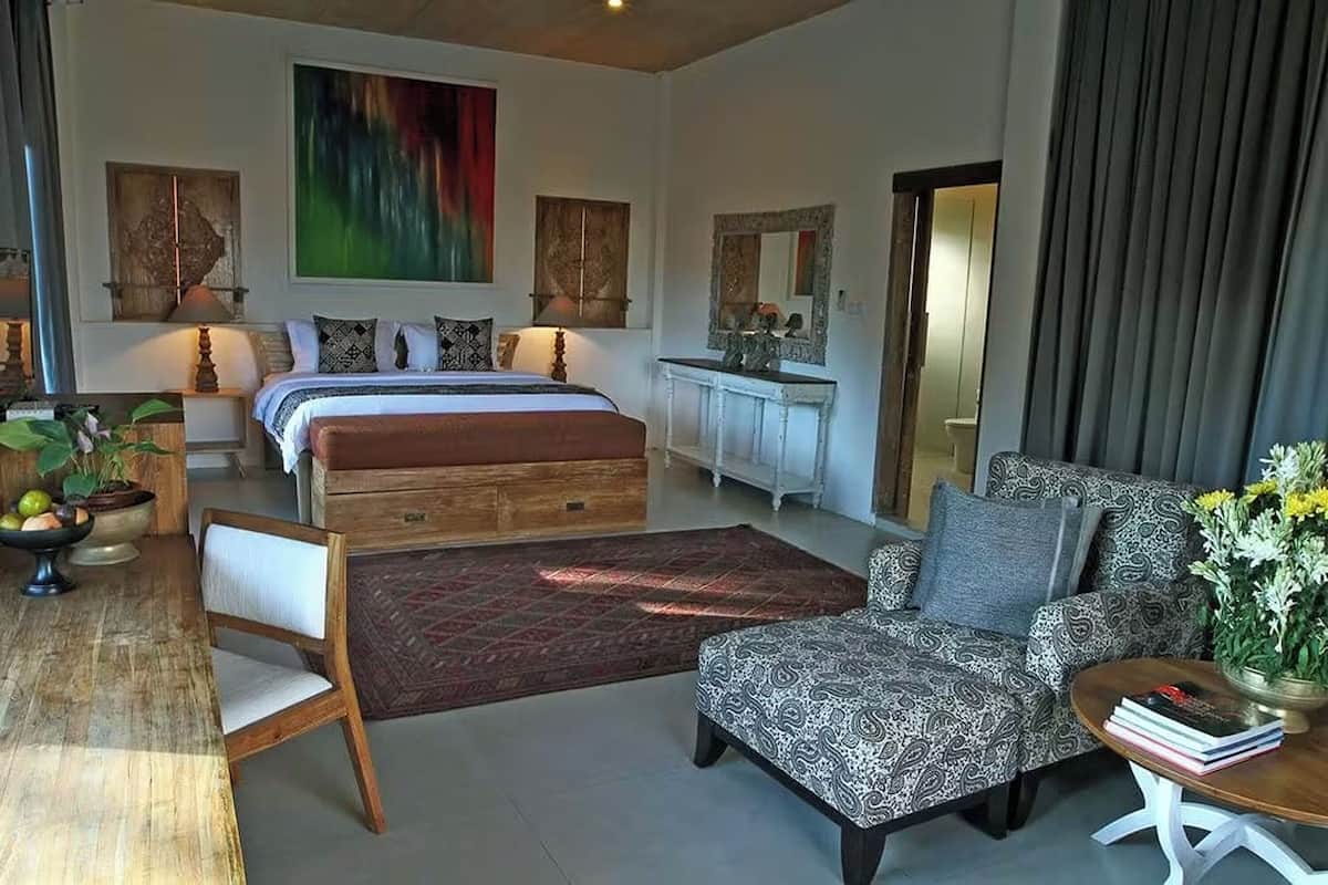 A modern bedroom with a large bed, a sofa, a dining table with chairs, and a fireplace.