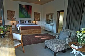 A bedroom with a bed, a sofa, a dining table with chairs, and a large painting on the wall. - Bangsring Breeze (Banyuwangi)