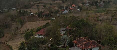 An aerial view of a rural area with a prominent mountain in the background, surrounded by fields and scattered houses with red roofs.