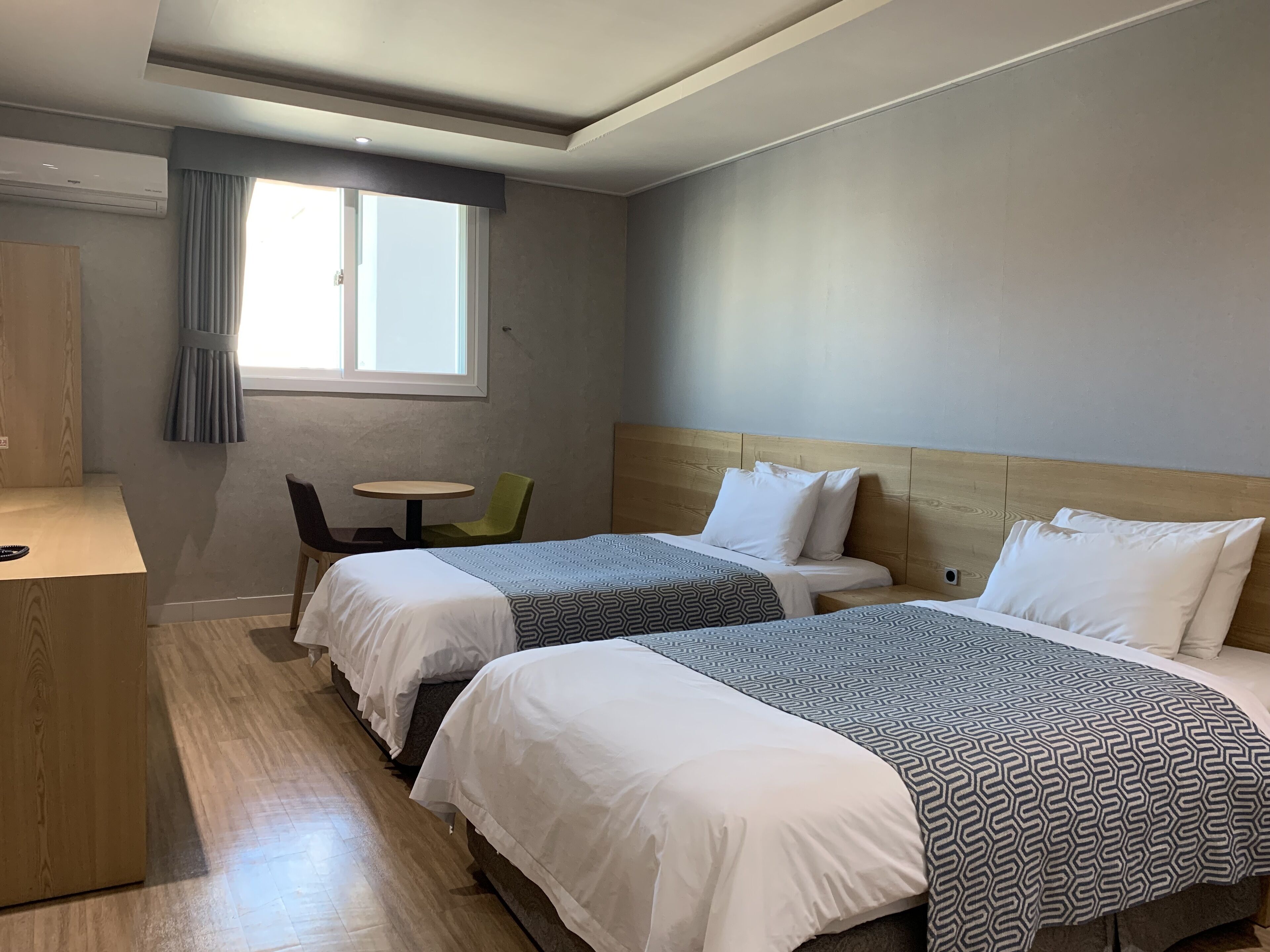 A hotel room with two beds, a small table, a chair, a desk, and a window with curtains.