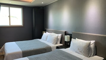 Habitación de hotel con dos camas, cada una con una colcha estampada, una mesita de noche con lámpara y una ventana que proporciona luz natural.