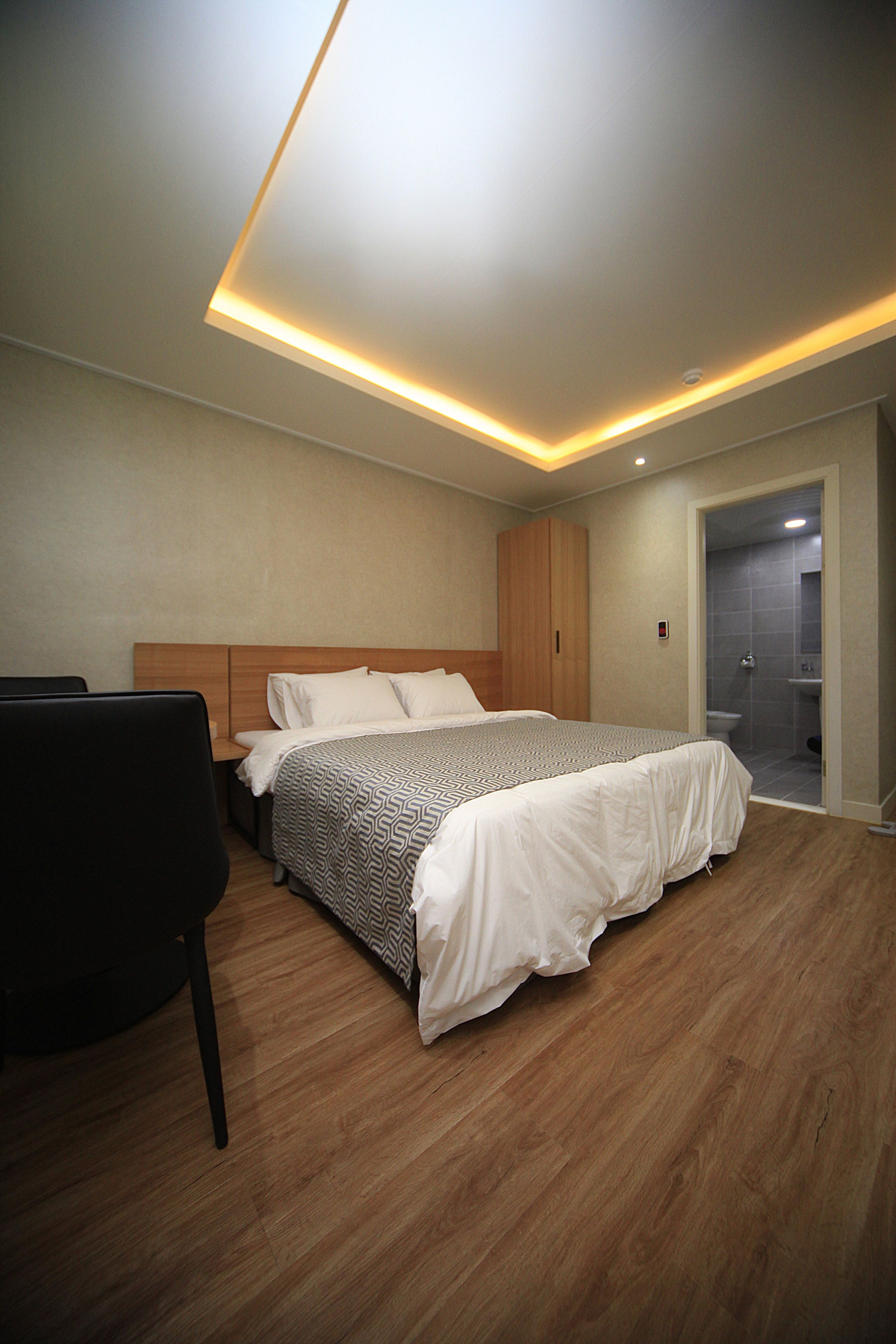 Un dormitorio moderno con una cama grande, un armario de madera y un baño separado visible a través de una puerta abierta.