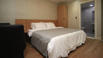 Un dormitorio moderno con una cama grande, un armario de madera y un baño separado visible a través de una puerta abierta.