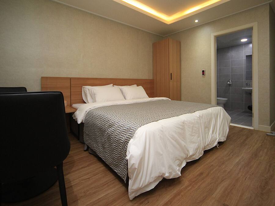 Un dormitorio moderno con una cama grande, un armario de madera y un baño separado visible a través de una puerta abierta.
