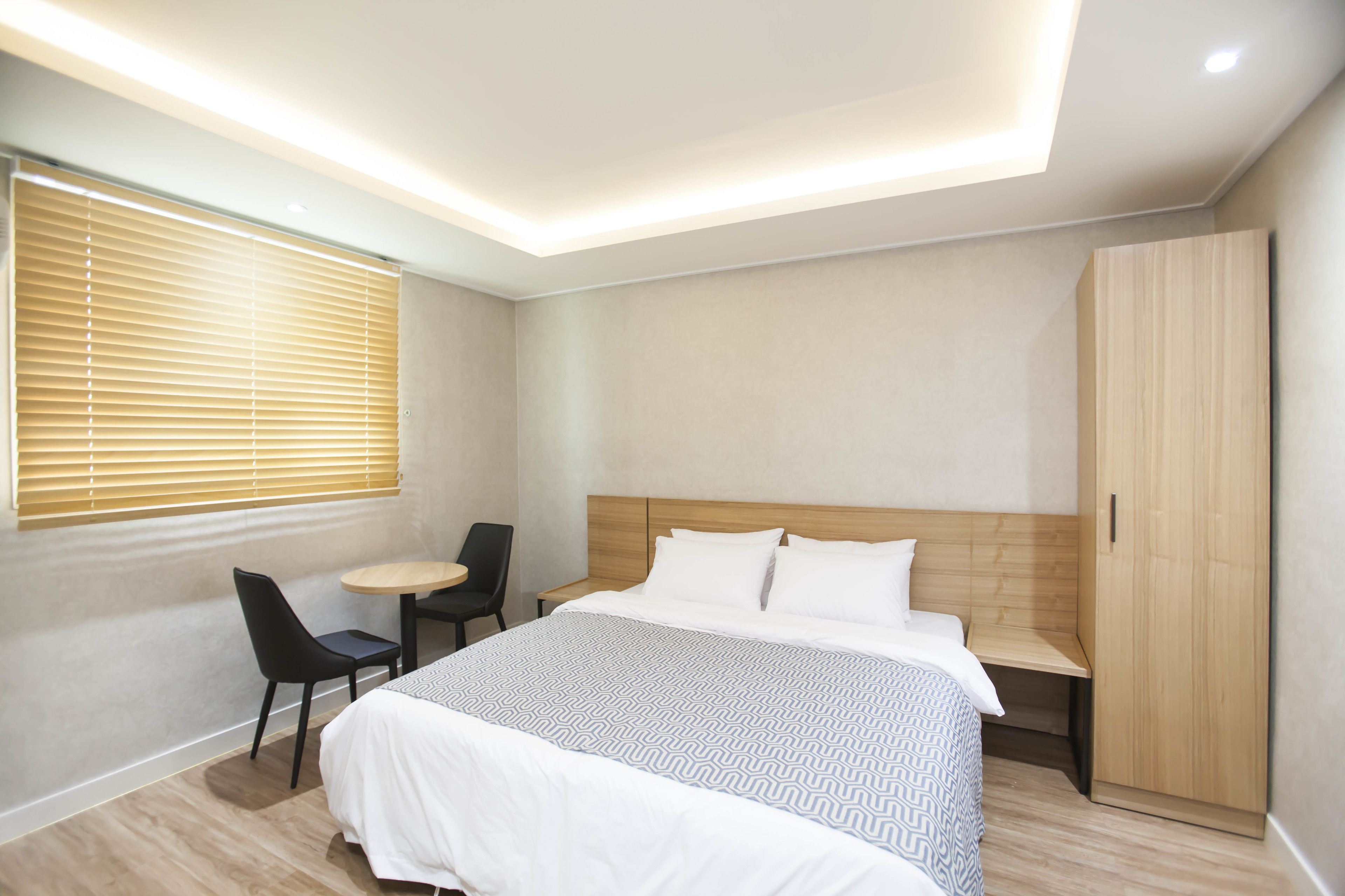 A modern hotel room with a large bed, a desk, a chair, and a wardrobe.
