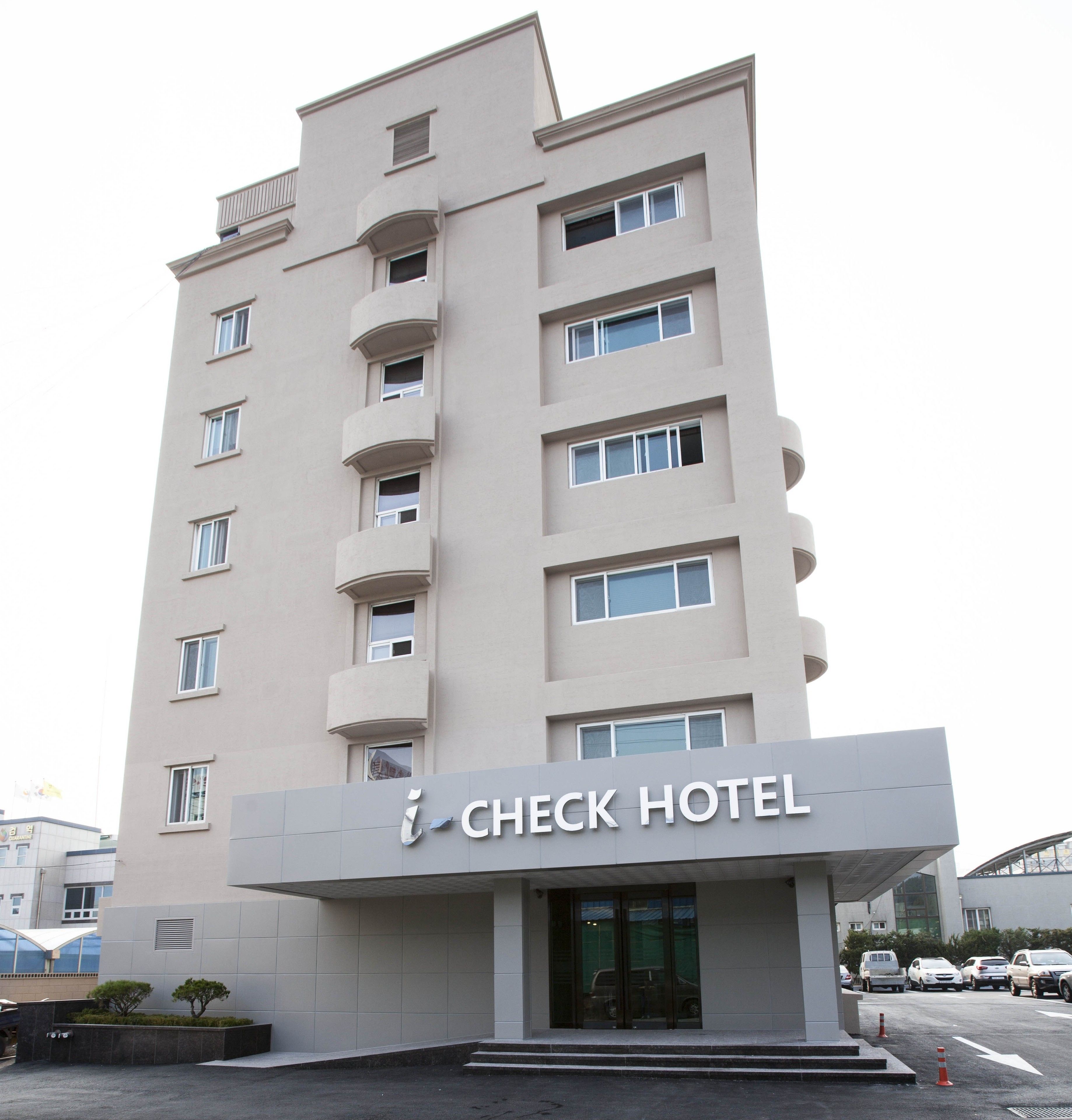 Um hotel moderno com fachada plana, várias varandas e uma entrada destacada com porta de vidro.