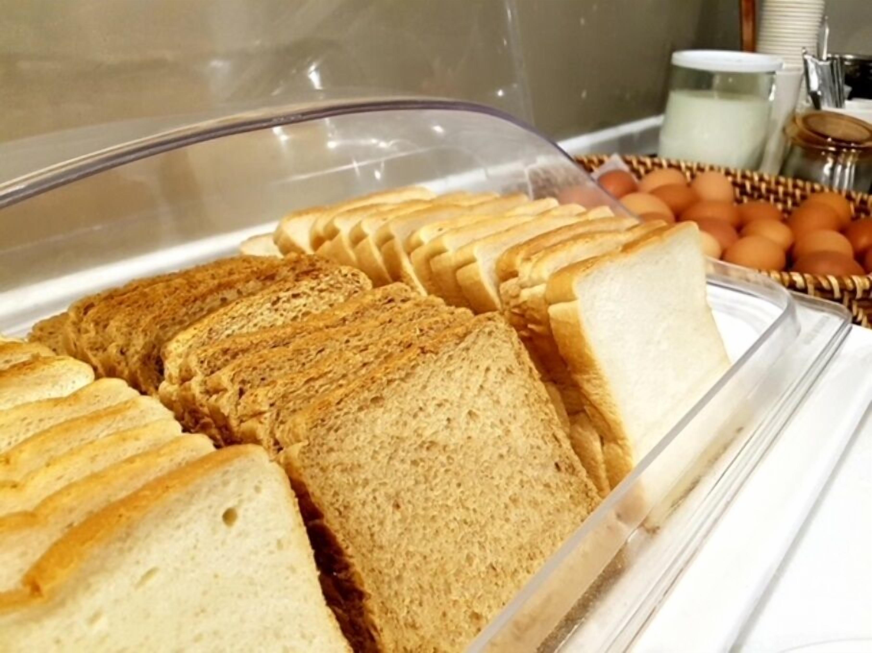A breakfast buffet with sliced bread, eggs, and a milk dispenser.