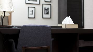 A hotel room with a desk, a lamp, a chair, and framed pictures on the wall.