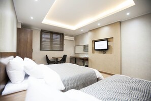 Habitación de hotel con dos camas, un escritorio, una silla, un televisor y un equipo de aire acondicionado.