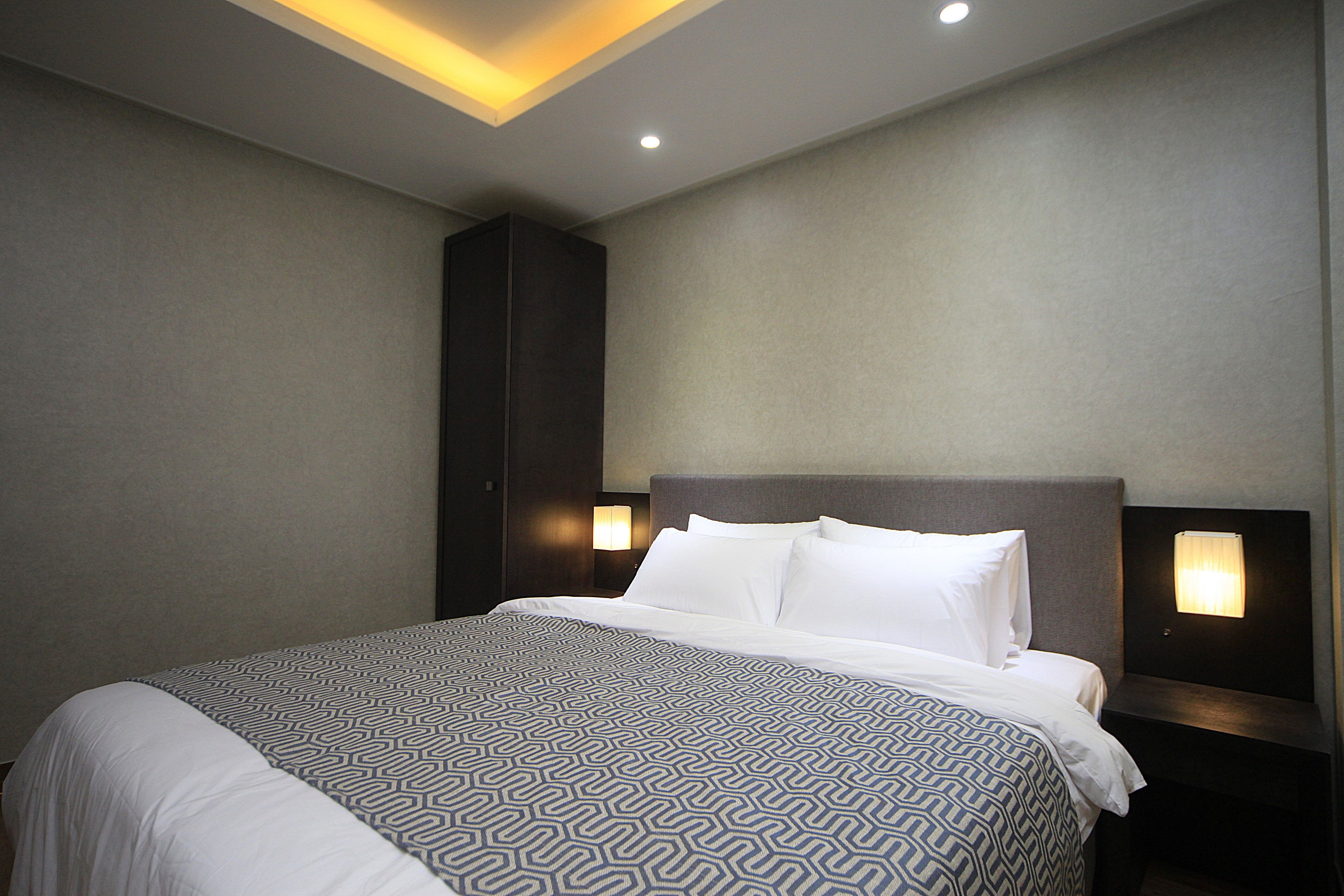 Una habitación de hotel con una cama grande, una mesita de noche con lámpara e iluminación en el techo.