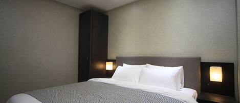Una habitación de hotel con una cama grande, una mesita de noche con lámpara e iluminación en el techo.
