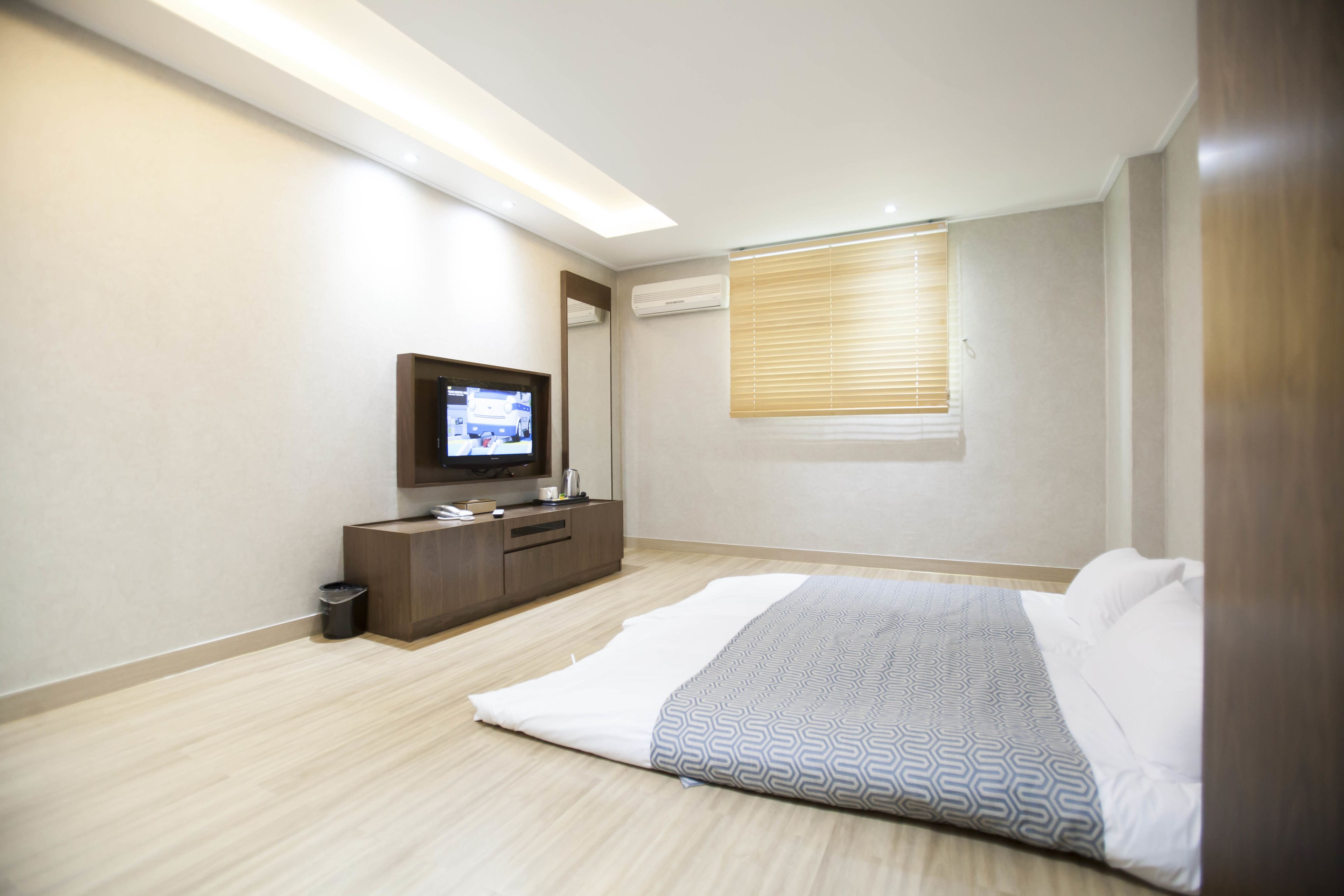 Un dormitorio moderno con cama, televisión, cómoda y ventana con persianas.