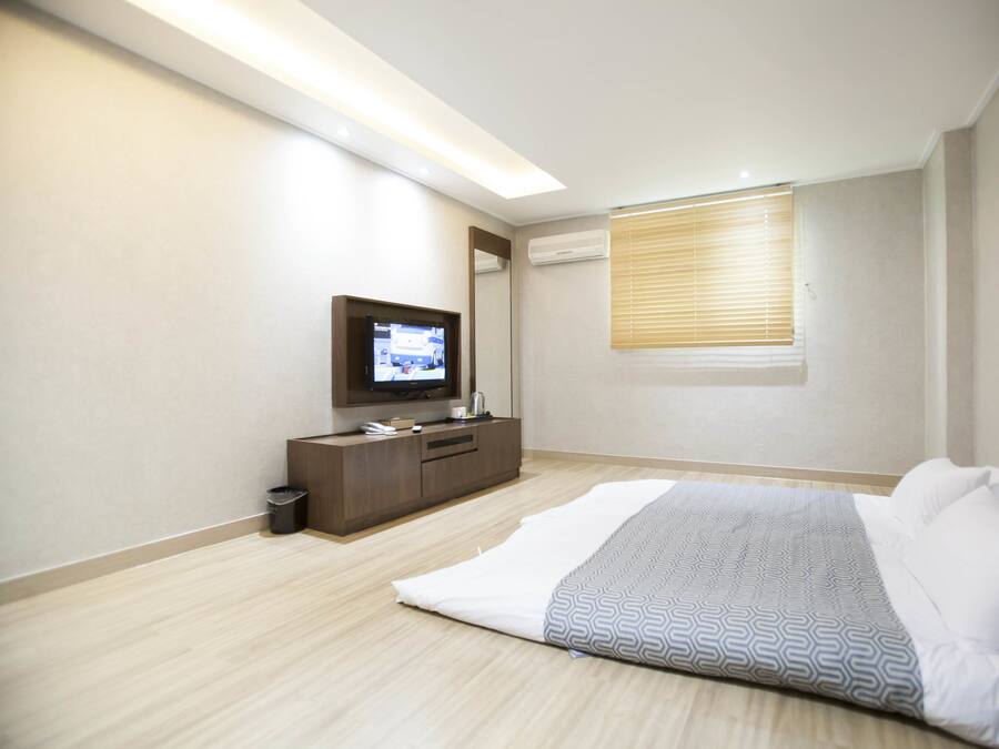 Un dormitorio moderno con cama, televisión, cómoda y ventana con persianas.