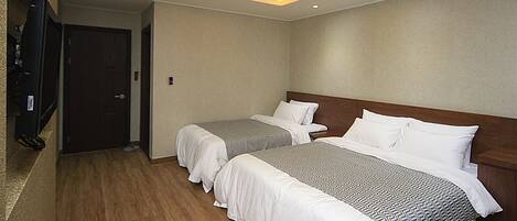 A hotel room with two beds, wooden flooring, a television, and recessed ceiling lighting.
