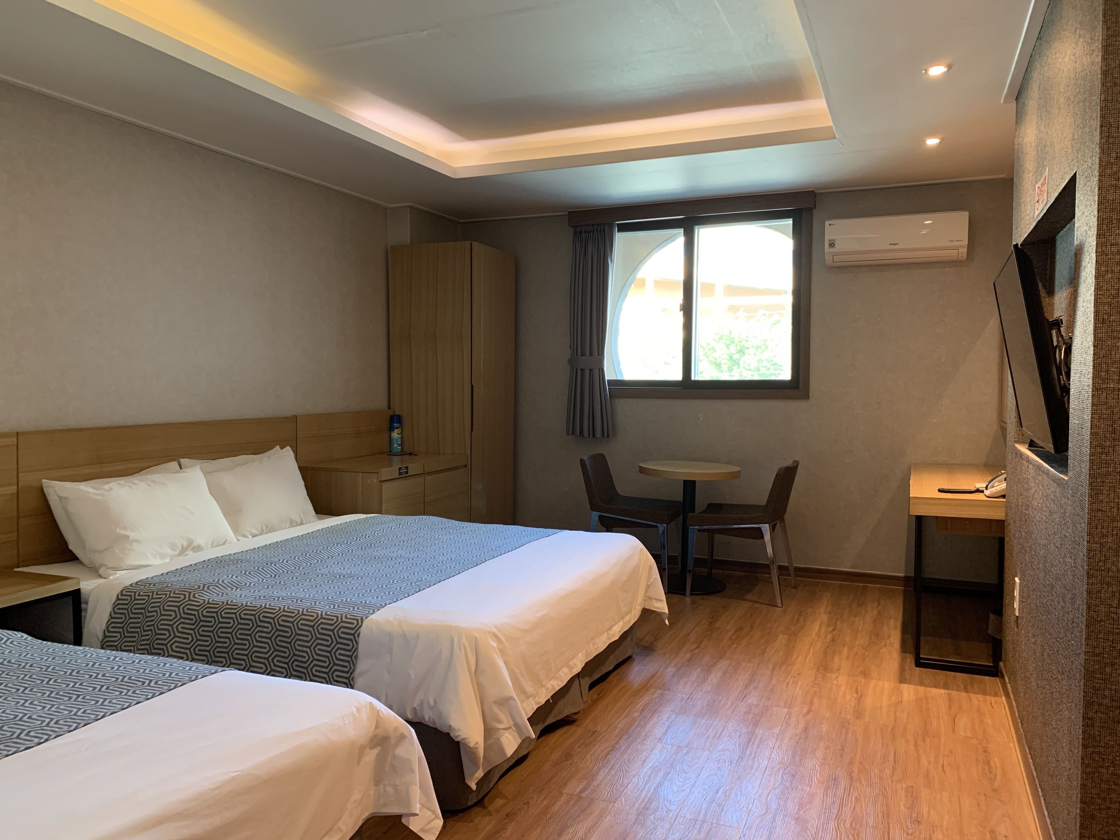 Une chambre d’hôtel avec deux lits, un bureau, une chaise, une petite table et une fenêtre avec des rideaux.