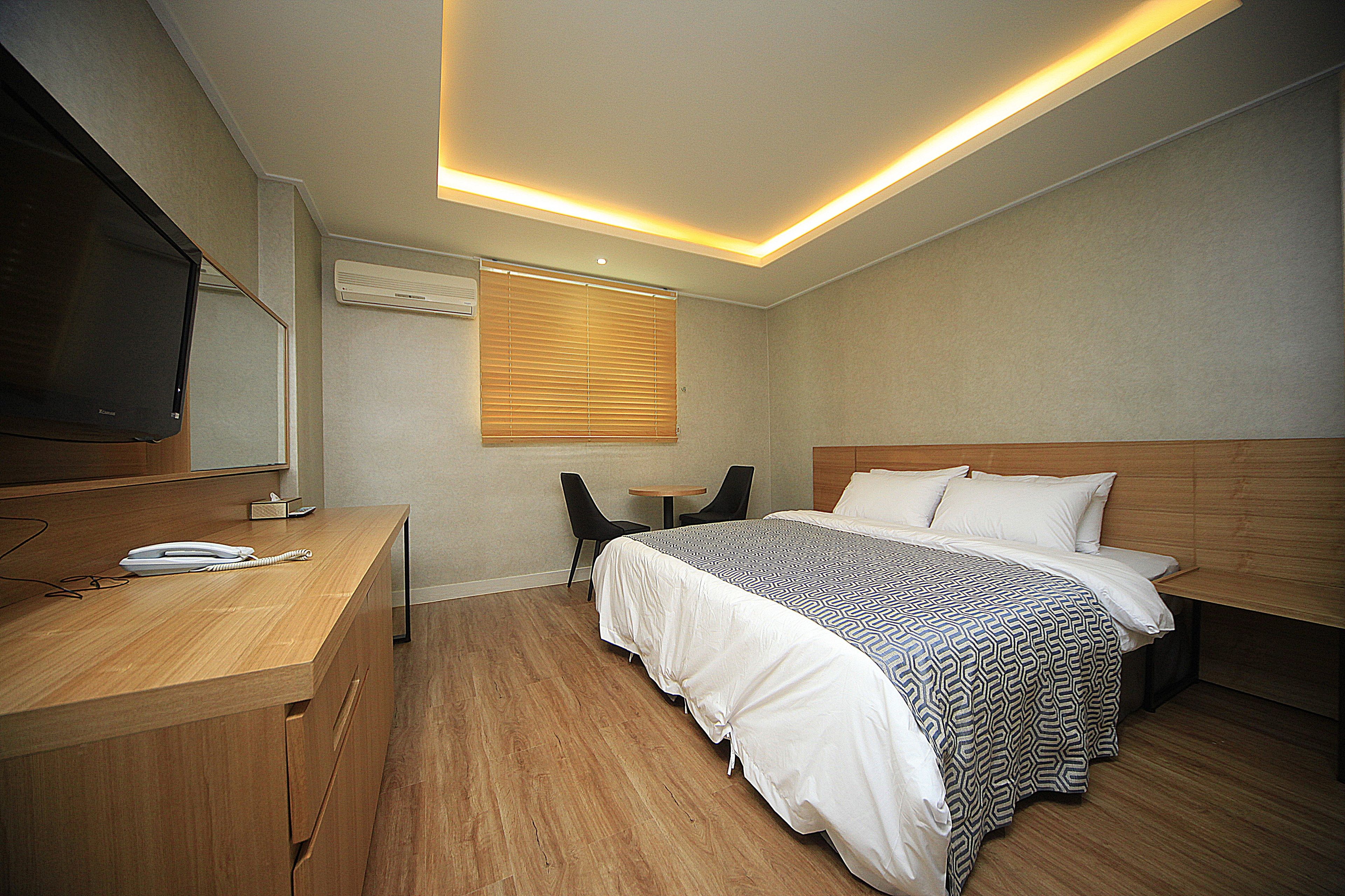 A hotel room with a bed, bedside table, desk, chair, and a television.