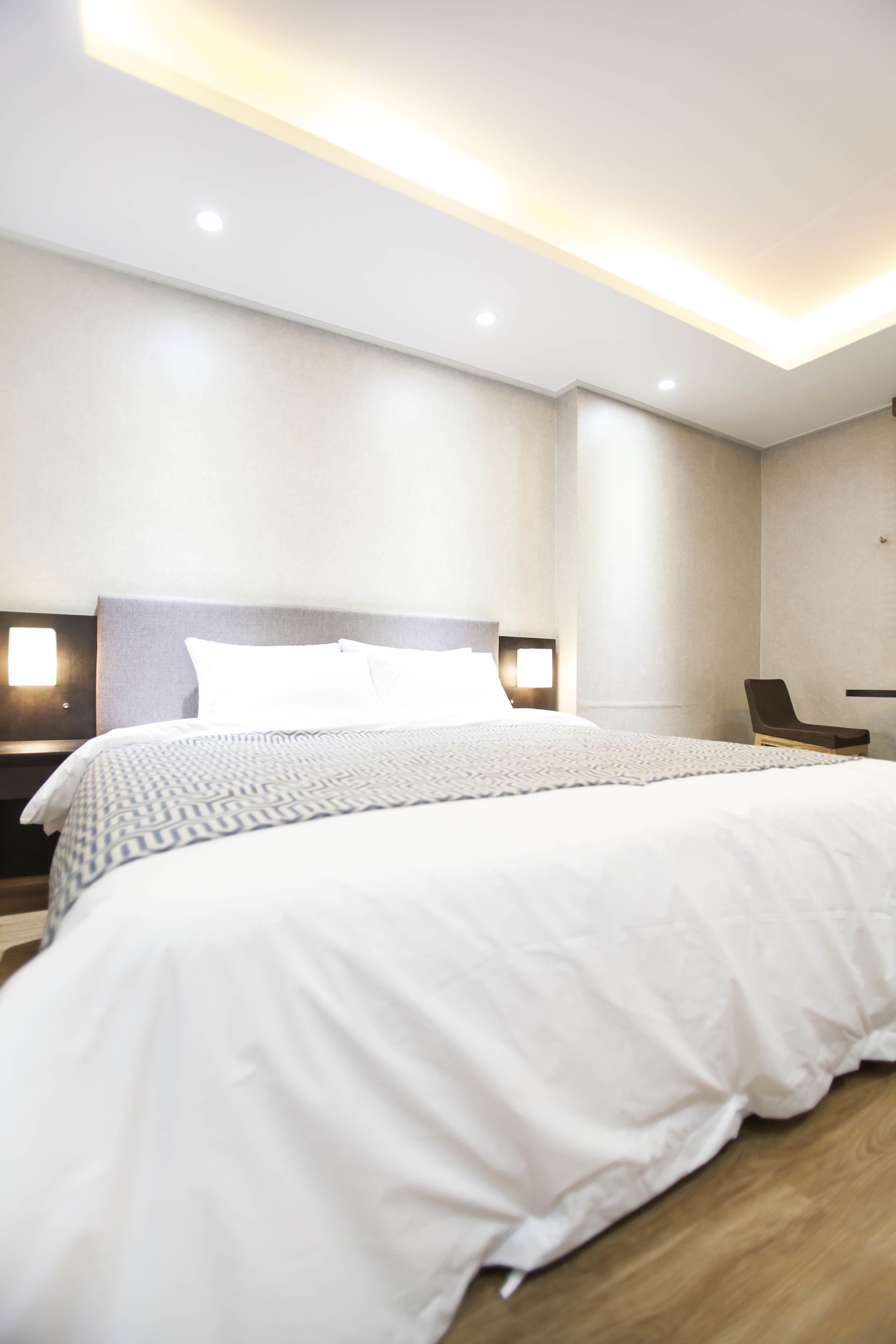 Habitació d'hotel moderna amb un llit gran, una tauleta de nit, una cadira i una làmpada penjada a la paret.