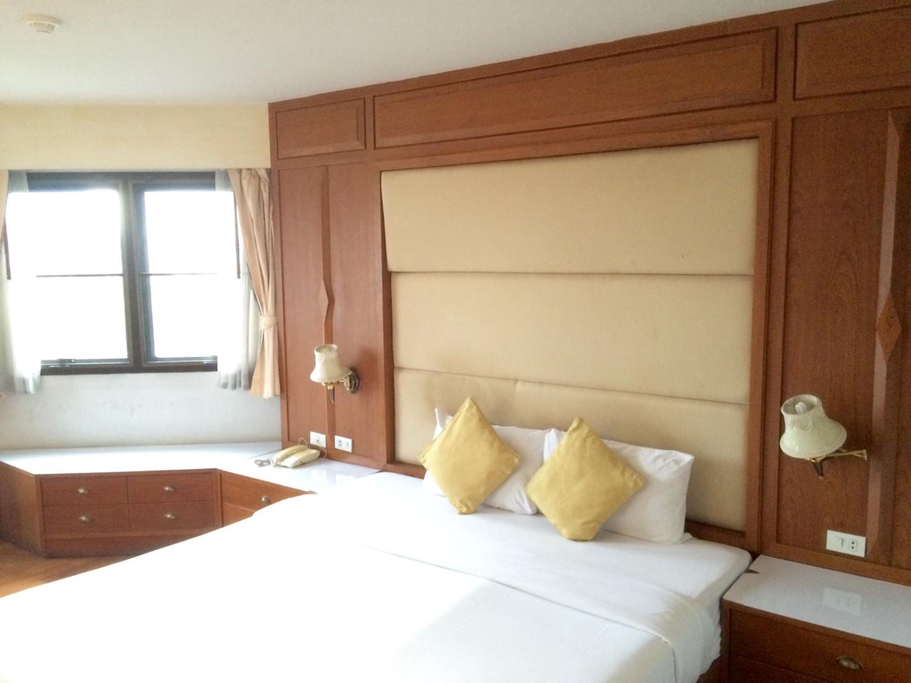 Quarto de hotel com uma cama grande, mesa de cabeceira, luminária e janela com cortinas.