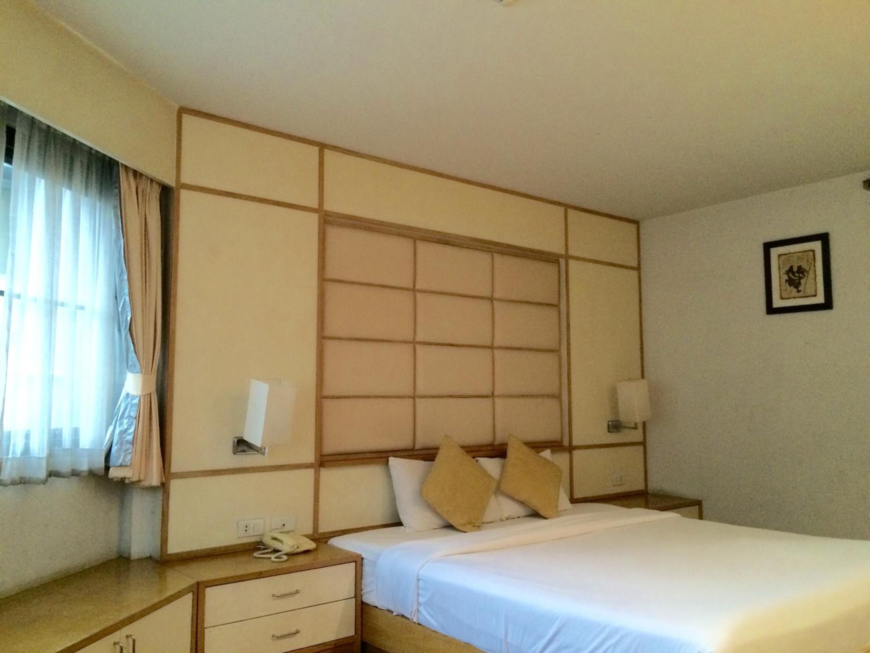 Una habitación de hotel con cama, mesitas de noche, teléfono y ventana con cortinas.