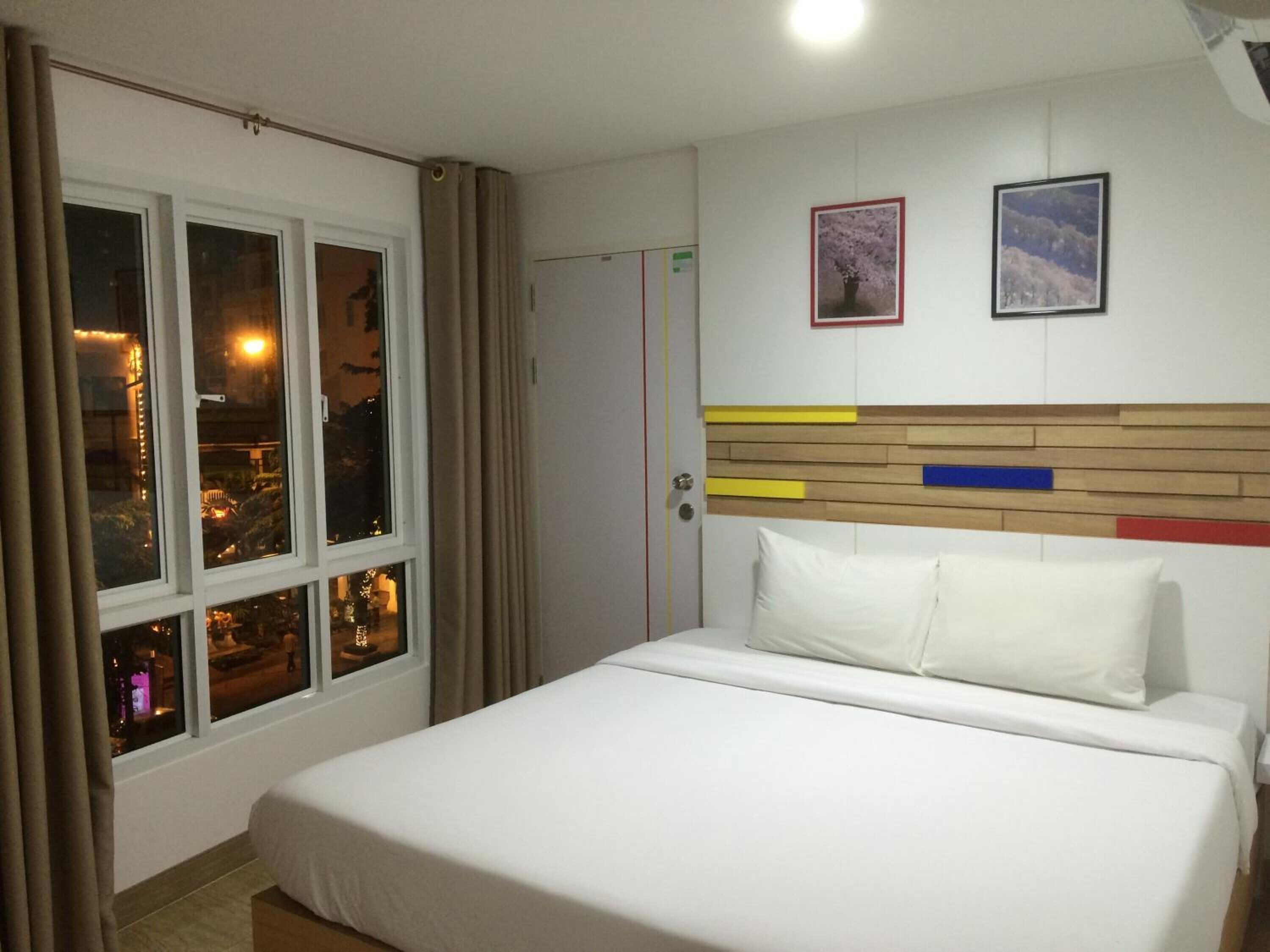 Habitación de hotel con una cama, una ventana con cortinas y dos cuadros en la pared.