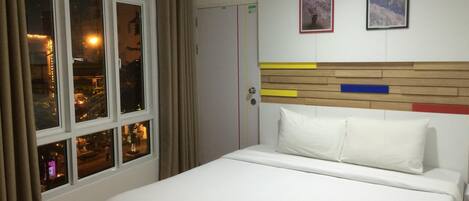 Habitación de hotel con una cama, una ventana con cortinas y dos cuadros en la pared.