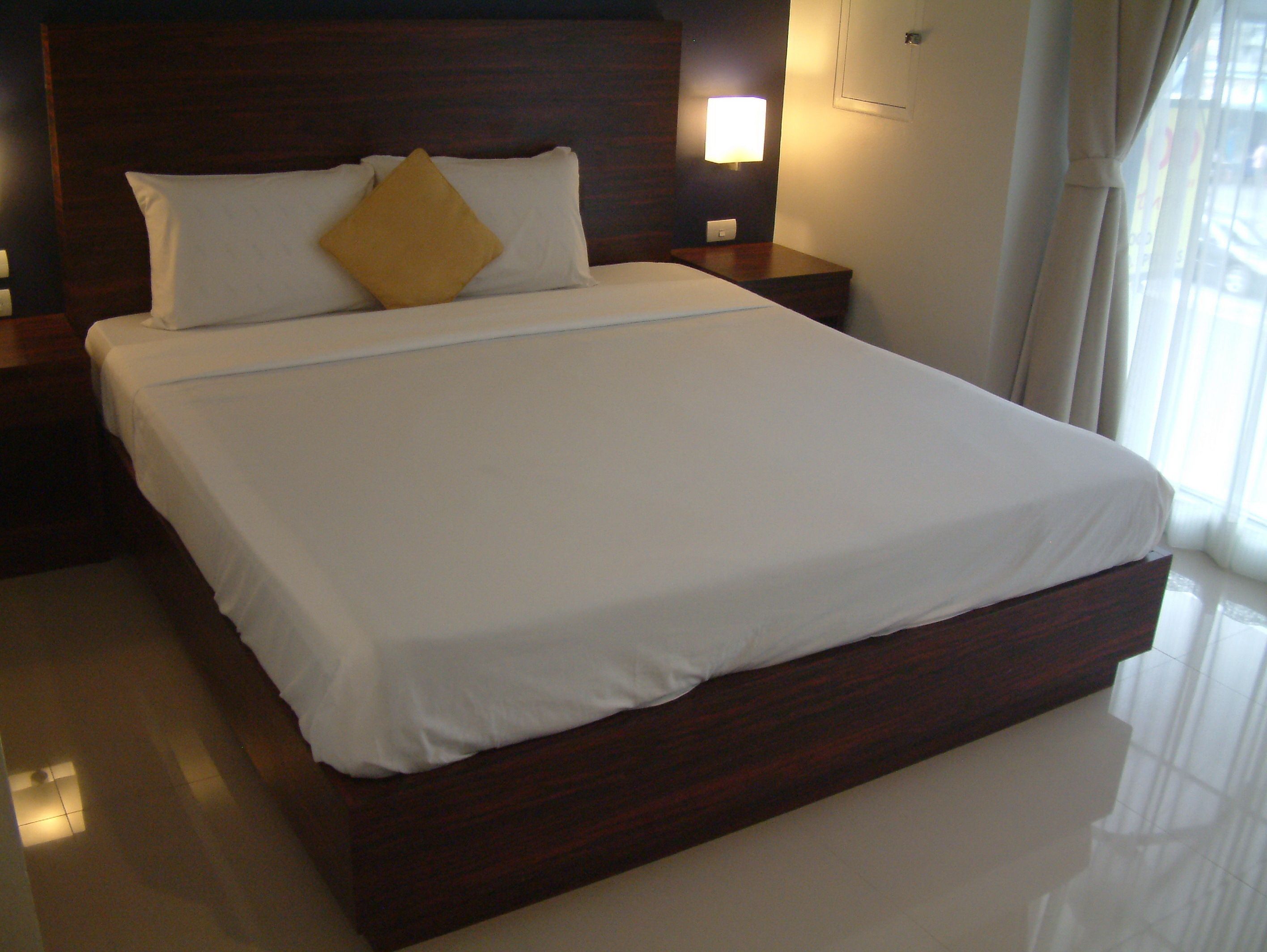Een net opgemaakt bed met witte lakens en één geel kussen in een hotelkamer.