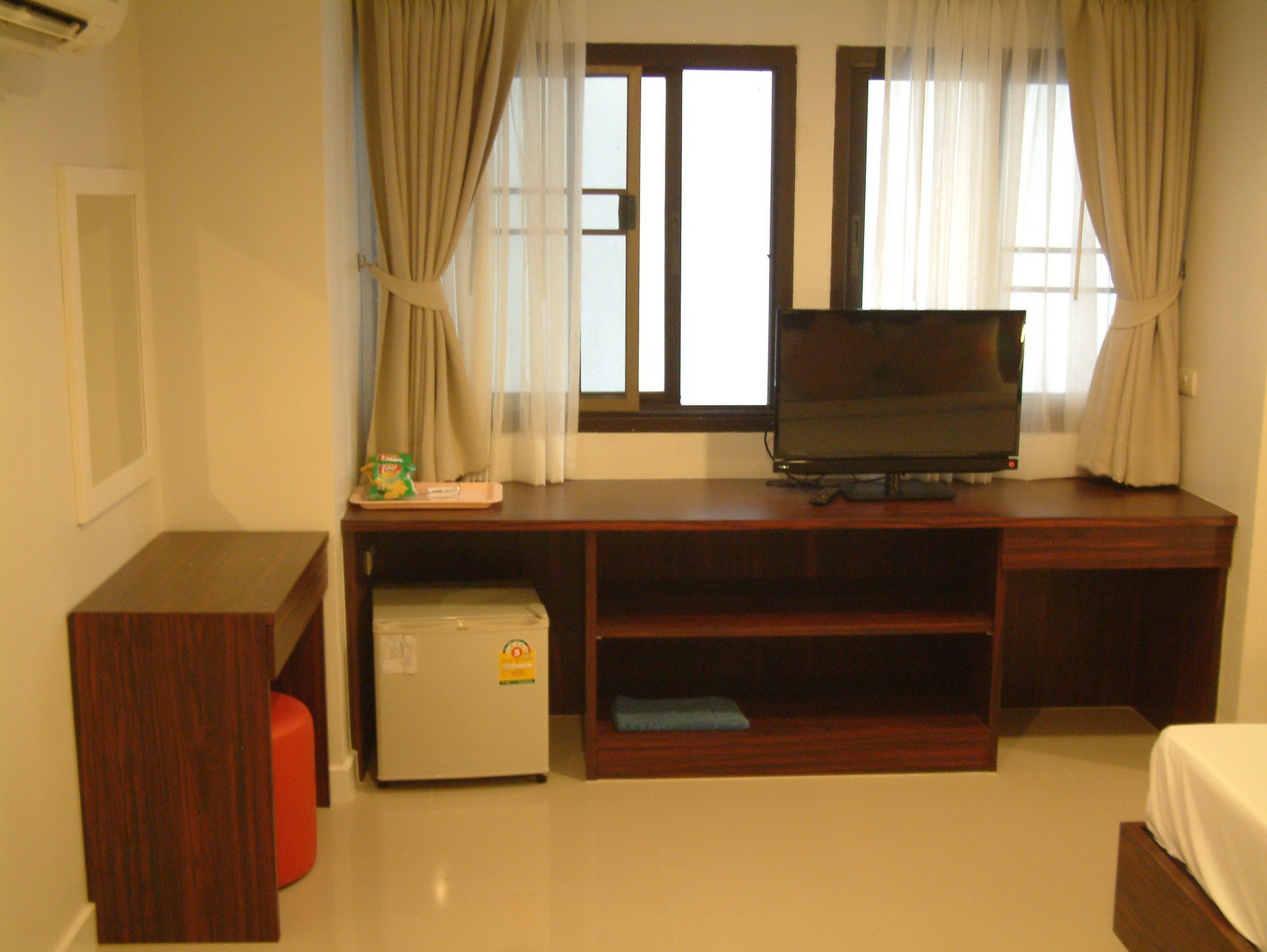 Habitación de hotel con un escritorio de madera, televisor, refrigerador pequeño y cama.