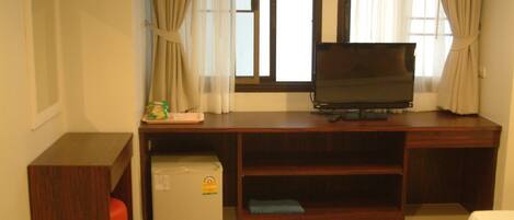 Habitación de hotel con un escritorio de madera, televisor, refrigerador pequeño y cama.