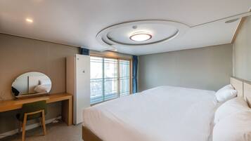 A bedroom with a bed, a desk, and a window.