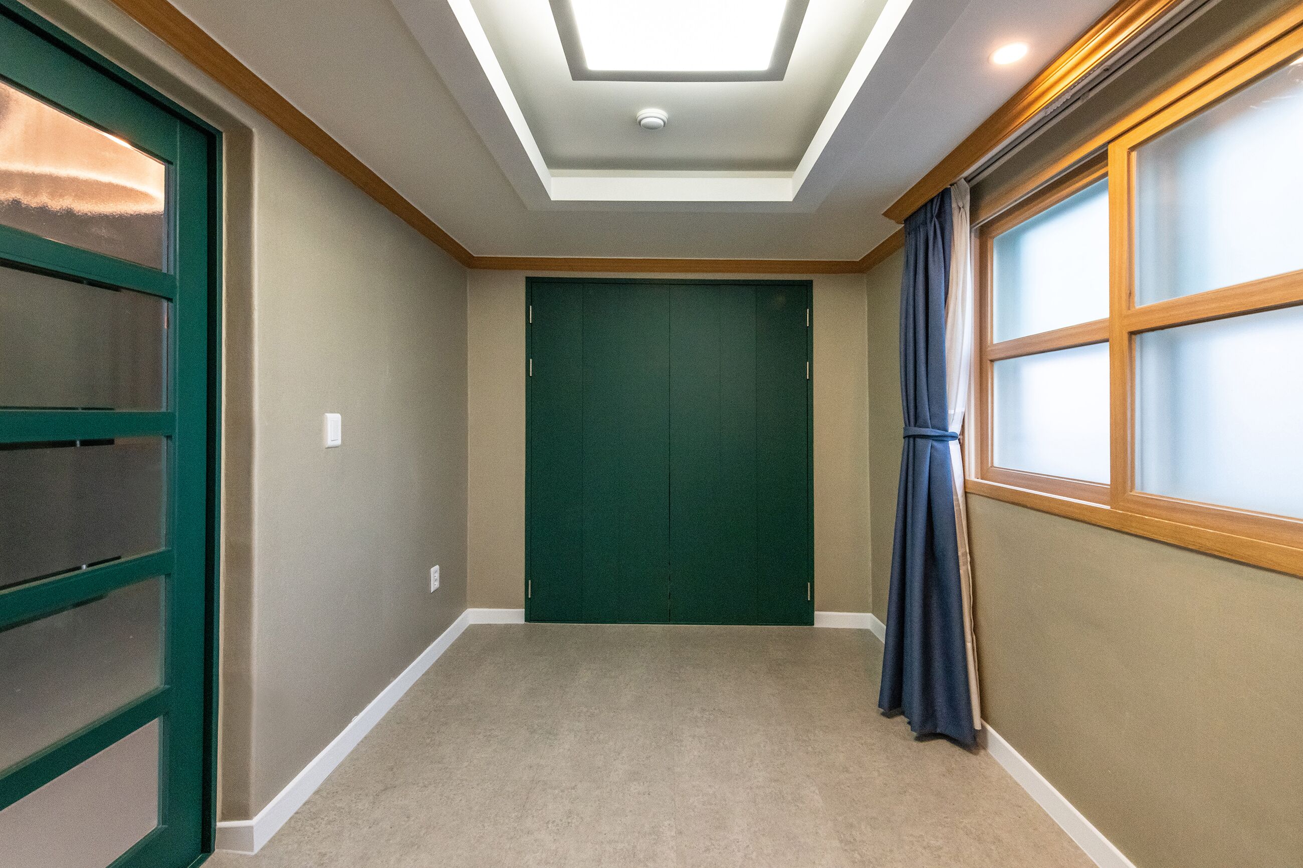 A hallway with a green door, a window with a curtain, and a ceiling light.