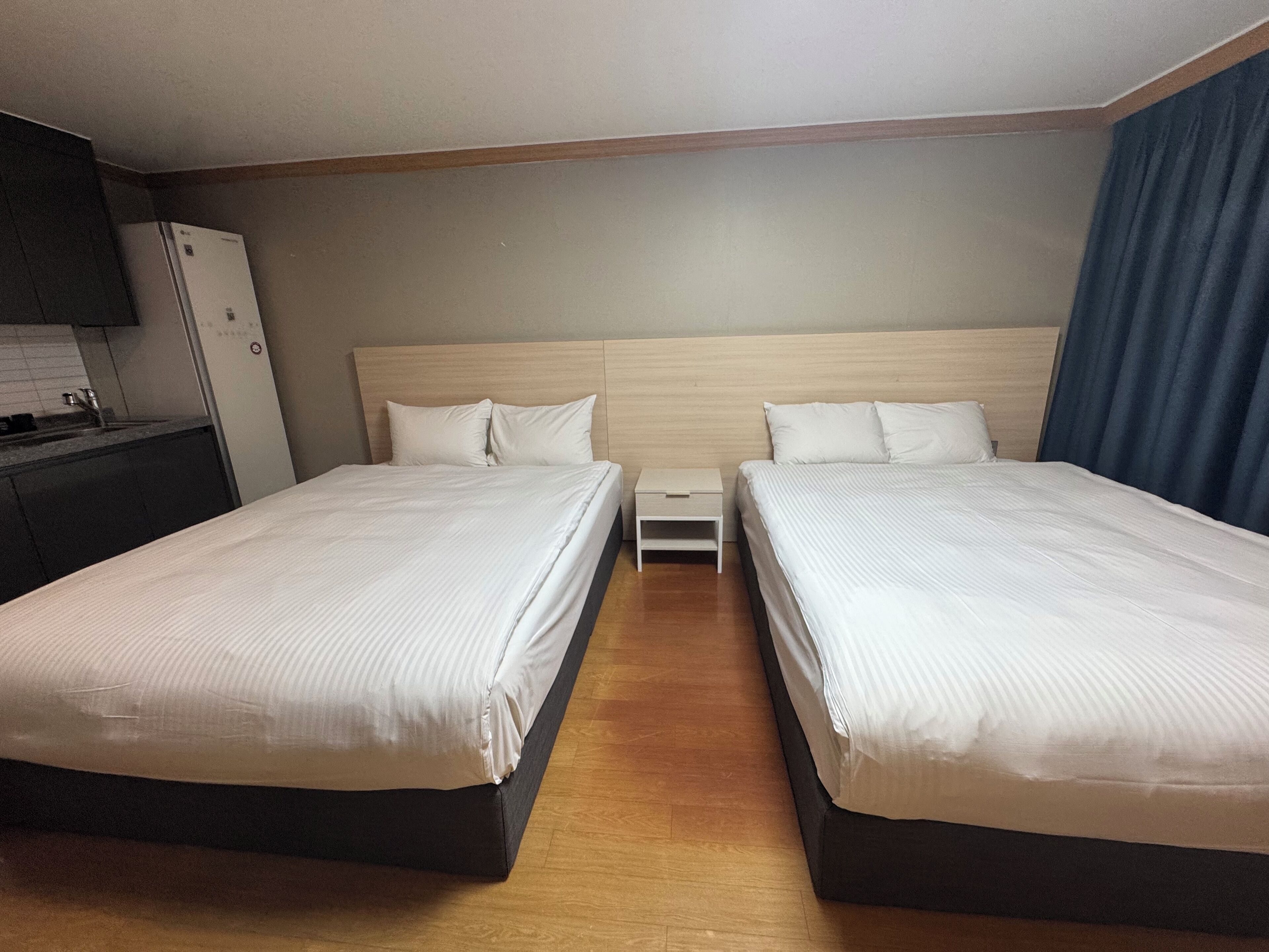A hotel room with two beds, a wooden headboard, a small bedside table, and a built-in TV.