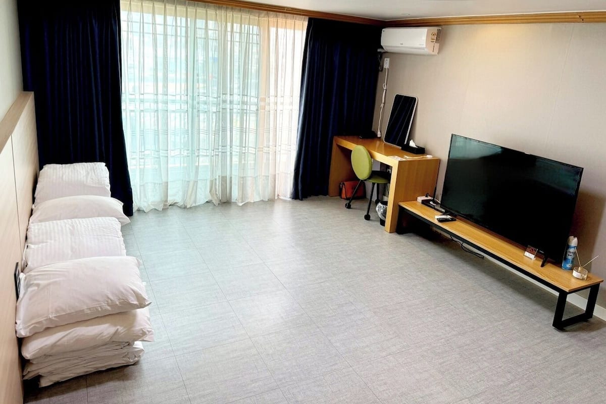 A hotel room with a bed, a desk with a computer, a TV, and a window with curtains.