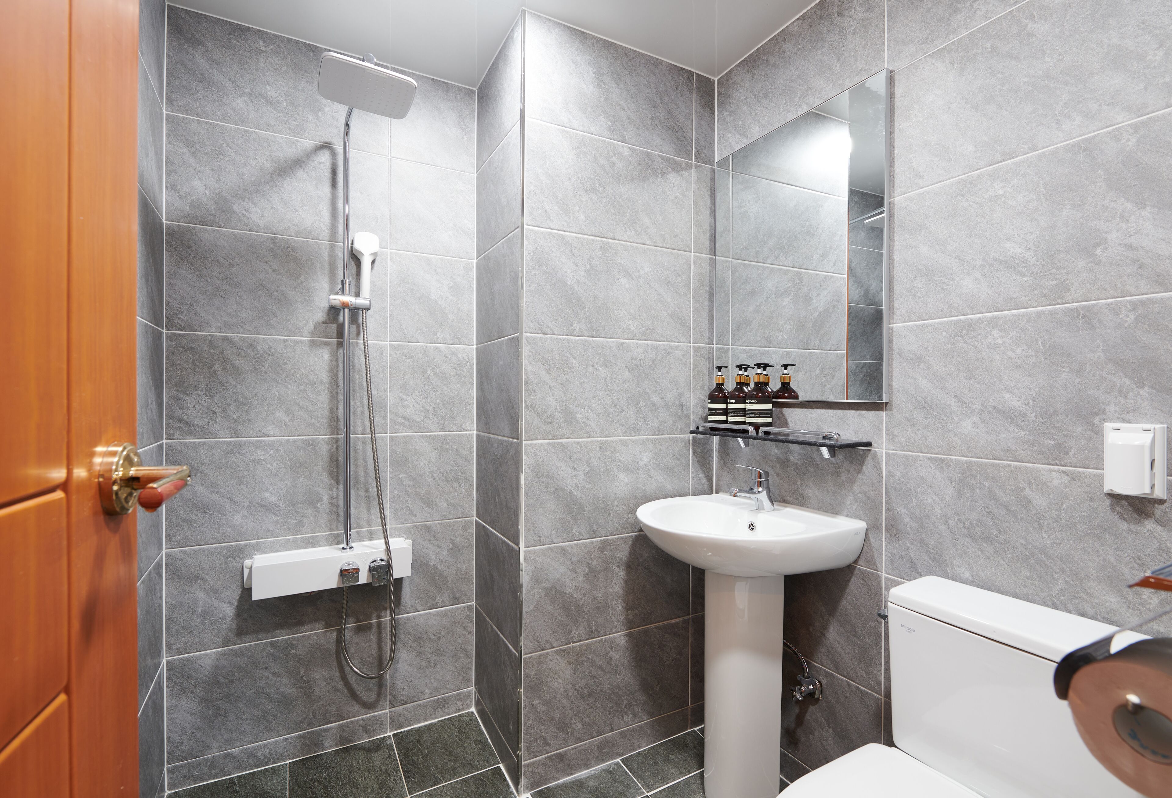 Un baño moderno con azulejos grises, un lavamanos blanco y una ducha.