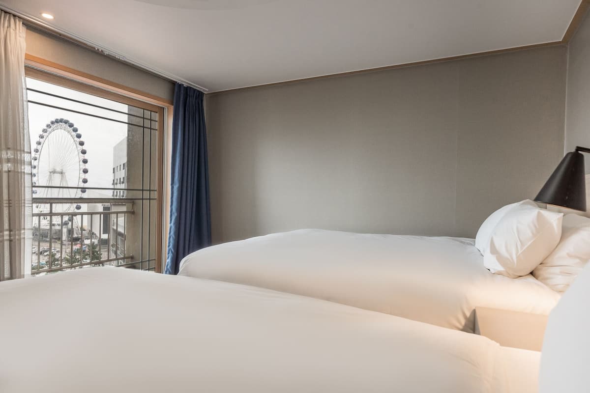 A hotel room with two beds, a large window with a view of a Ferris wheel, and a balcony.