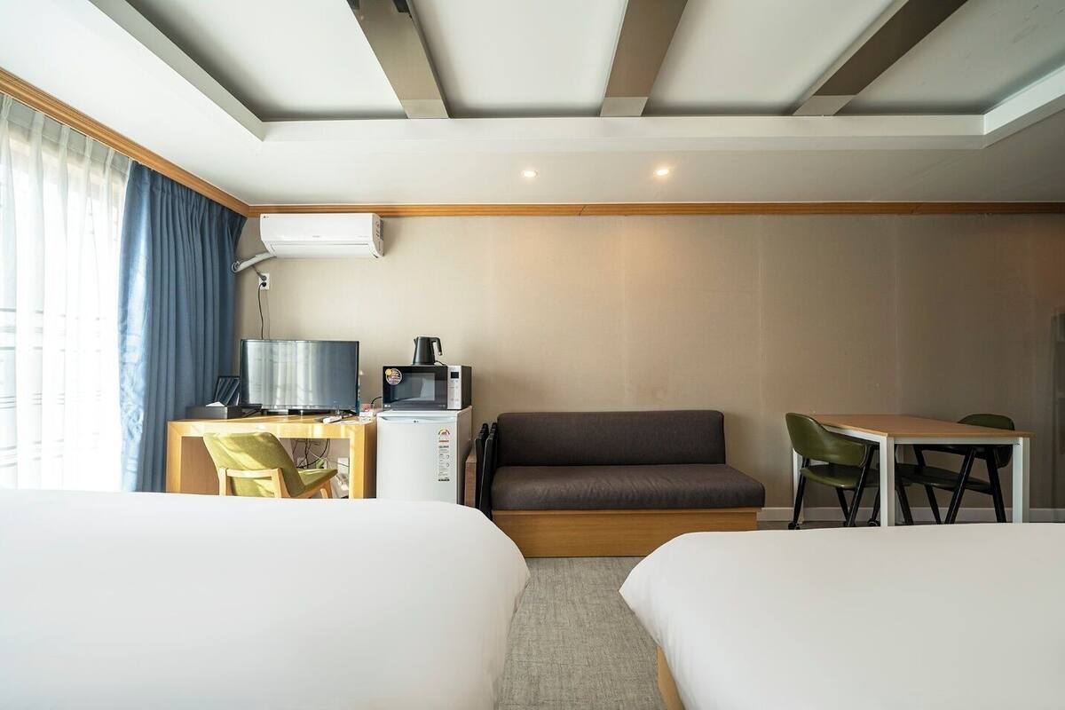 A hotel room with two beds, a desk with a computer and a coffee maker, a sofa, and a dining table with chairs.