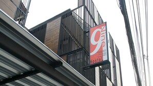 A hostel with a sign indicating it offers dormitory rooms and private rooms, a contact number, and a view of the street with a parked car. - 9 Hostel - Hostel (Chiang Mai)