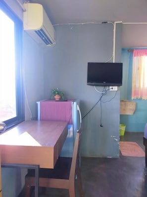 A room with a wooden table, a television mounted on the wall, and a window with curtains. - 9 Hostel - Hostel (Chiang Mai)