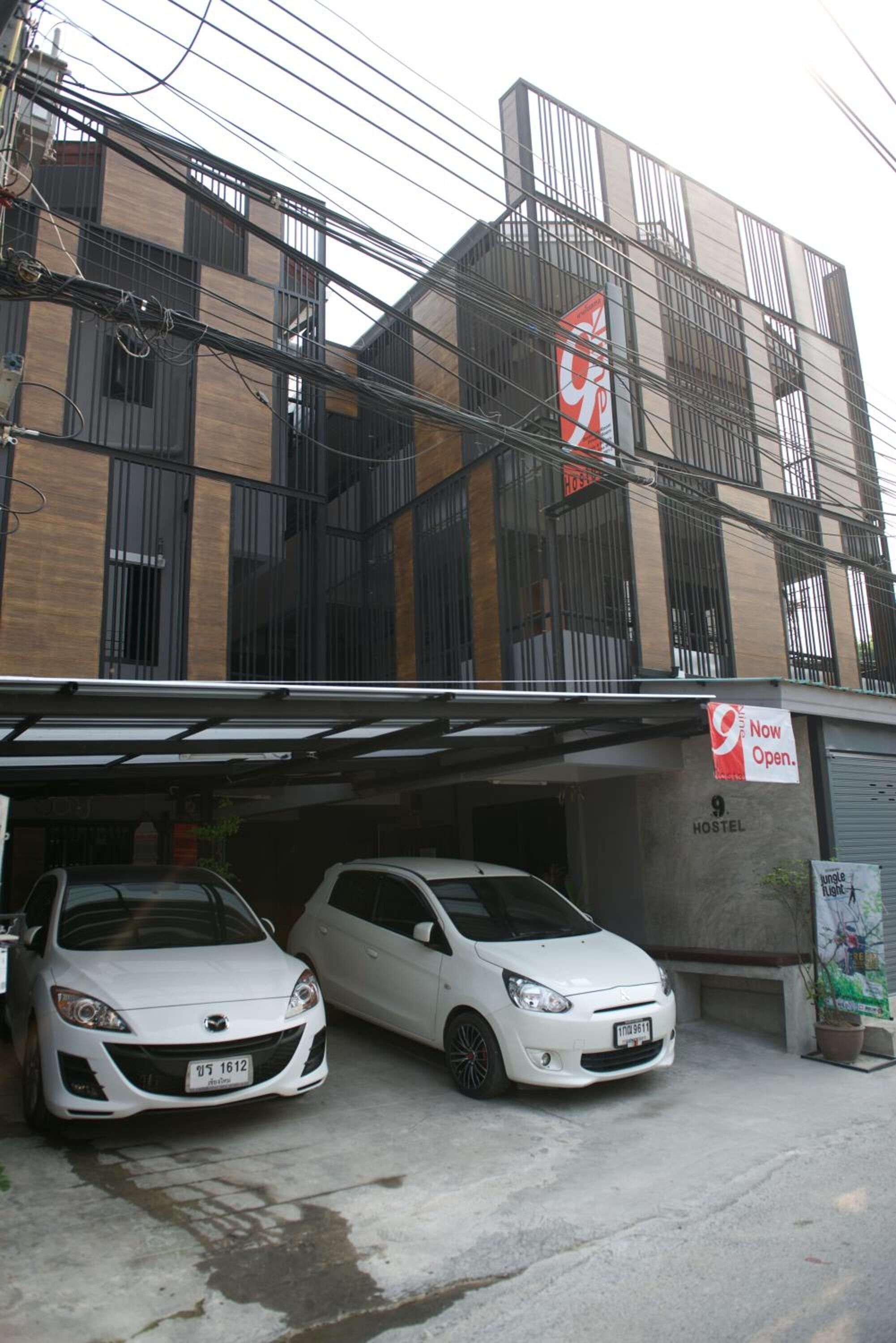 A hostel with two white cars parked in front, a sign indicating it's now open, and a large red and white sign on the building.