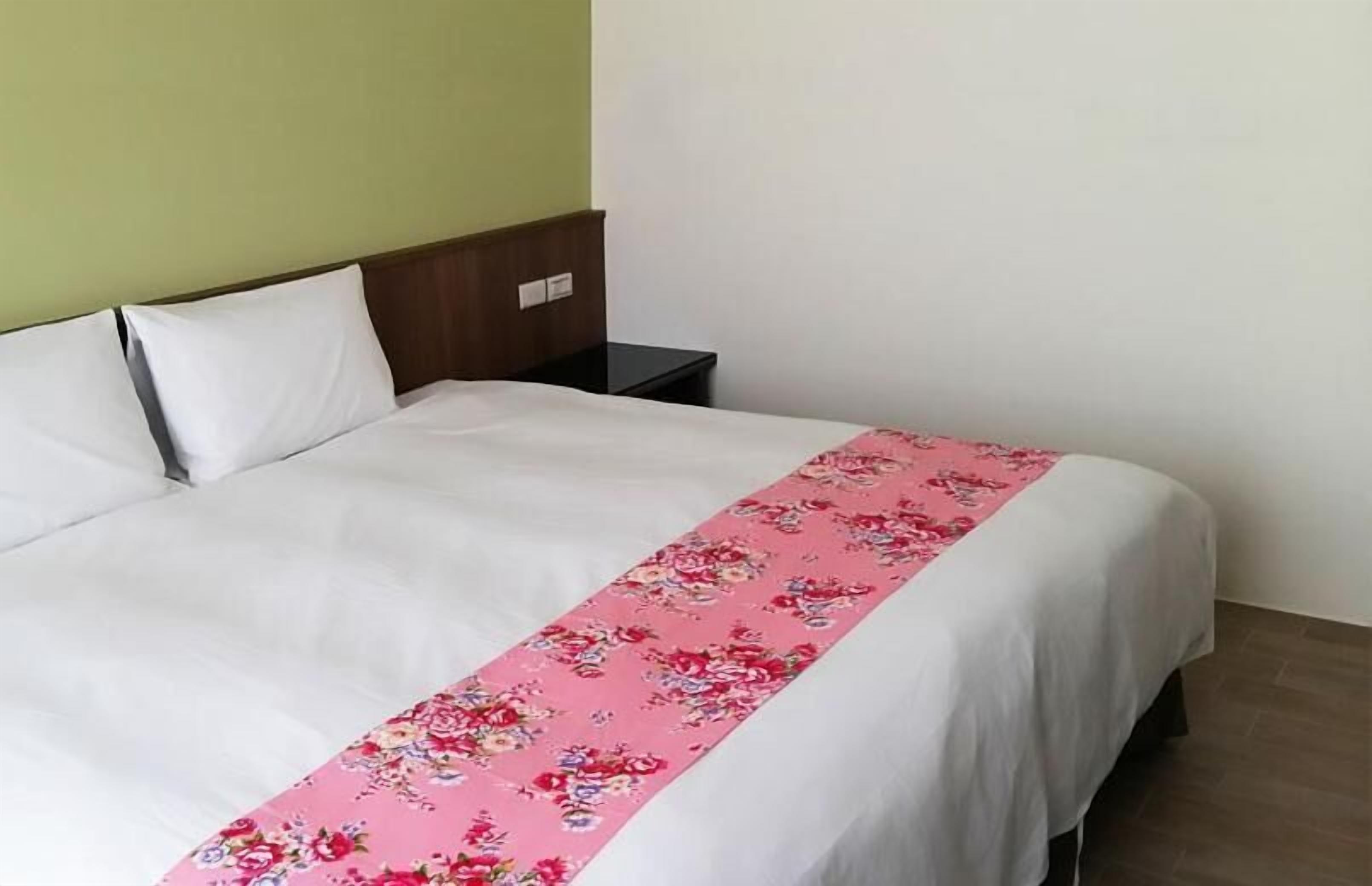 Una cama individual con una colcha blanca y un corredor floral rosa.