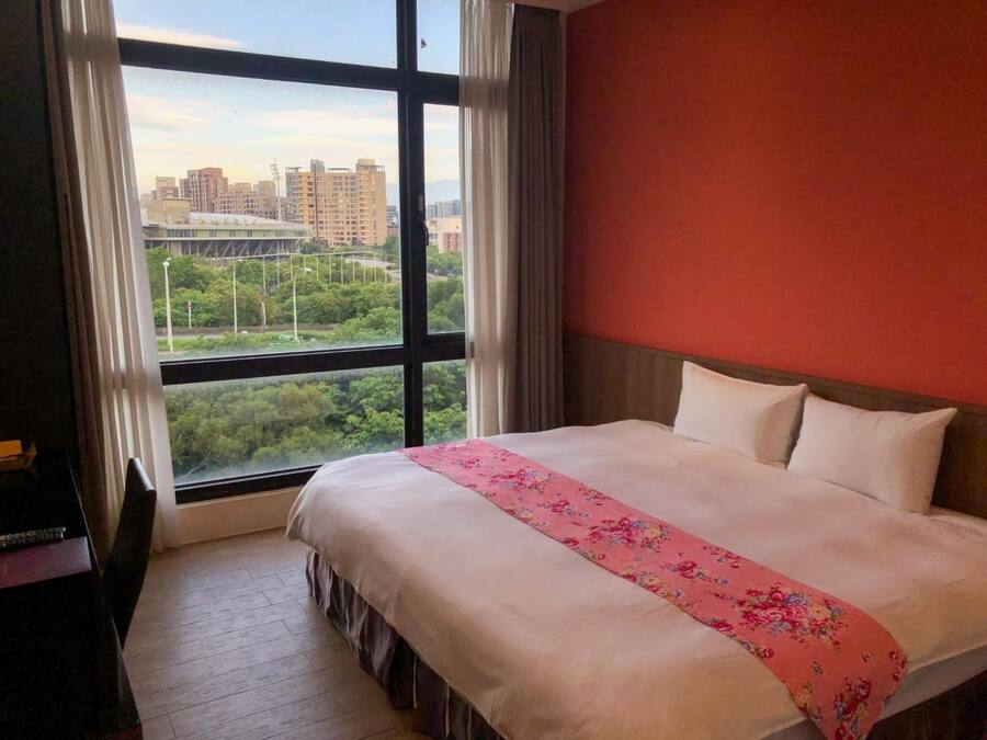 Habitación de hotel con un ventanal grande, una cama con ropa blanca y una pared roja.
